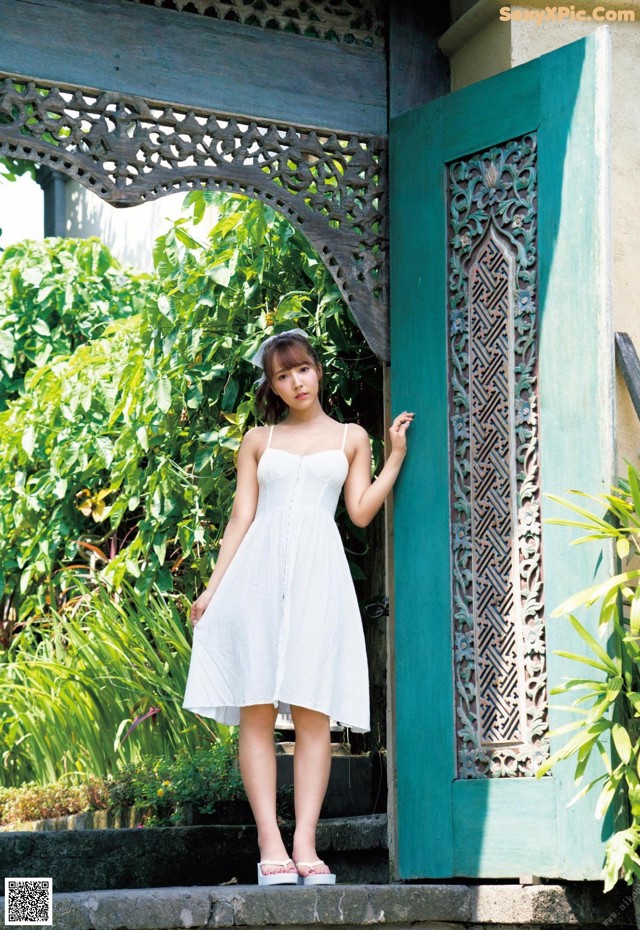 A woman in a white dress standing in front of a blue door.