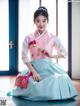 A woman in a pink and blue hanbok sitting on the floor.