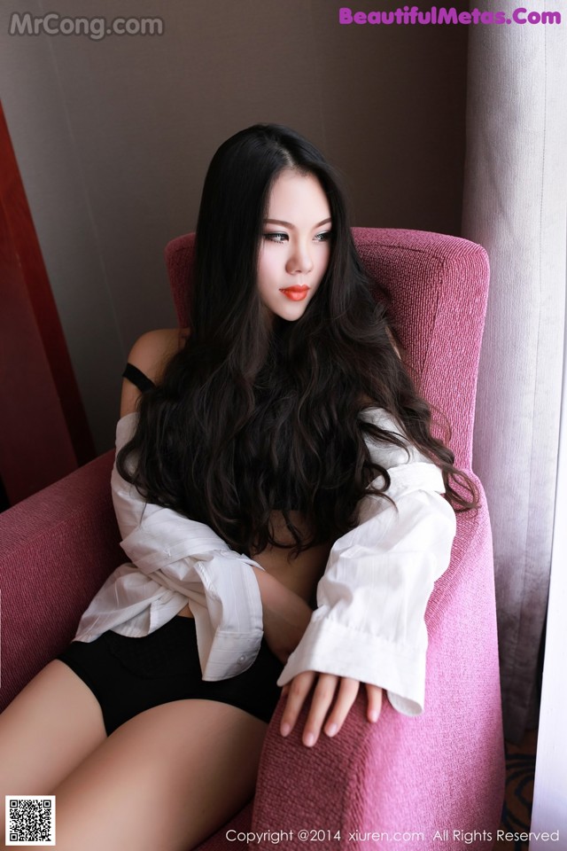 A woman sitting on a pink chair in a room.