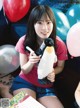 A woman holding a stuffed penguin in front of balloons.