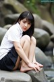 A woman sitting on top of a rock next to a river.