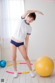 A woman in a white shirt and blue panties standing next to a yellow ball.