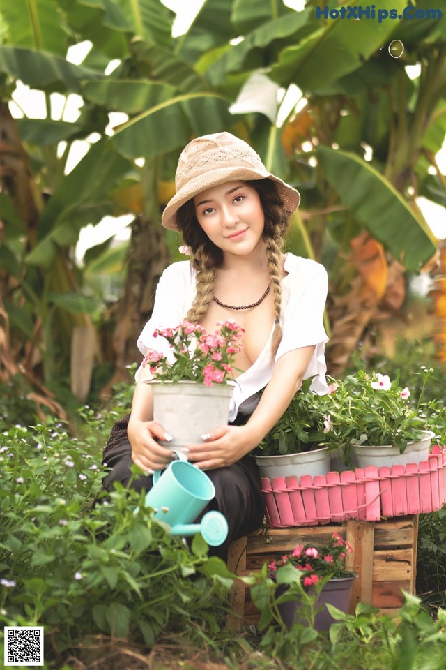 A woman sitting in a garden holding a watering can.