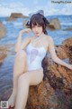 A woman in a white bathing suit sitting on a rock by the ocean.