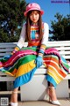 A woman sitting on a white bench wearing a colorful dress and hat.